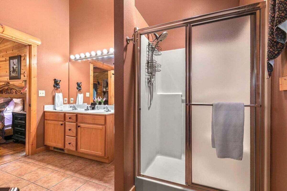 A bathroom with a wooden vanity, a glass shower enclosure, and a mirror with lights.
