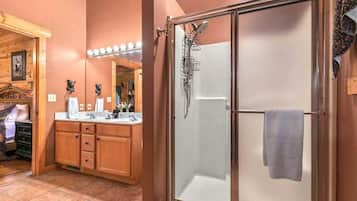 A bathroom with a wooden vanity, a glass shower enclosure, and a mirror with lights.