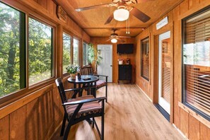 Un interior de madera con ventilador de techo, una mesa de comedor con sillas y ventanas amplias.