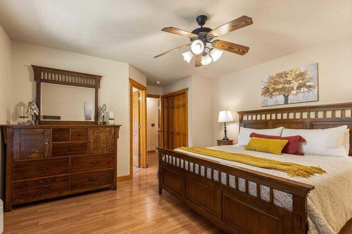 Een slaapkamer met een houten bed, een dressoir, een plafondventilator en een schilderij aan de muur.