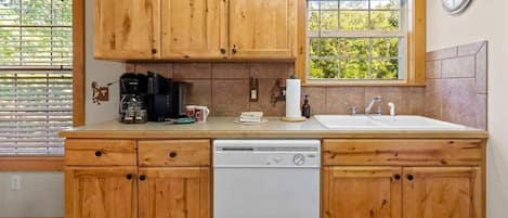Una cocina con armarios de madera, lavavajillas, cafetera y una ventana con persianas.