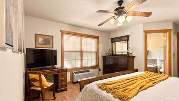 A bedroom with a bed, a desk, a chair, a ceiling fan, and a window with blinds.