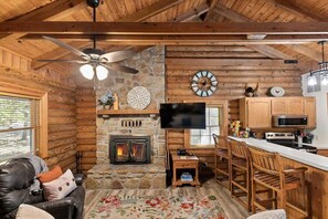 A log cabin interior with a fireplace, a television, wooden furniture, and a stone wall. - Genuine Log Cabin, Jetted Tub, Gas Fireplace, Endless Community Amenities (Branson)