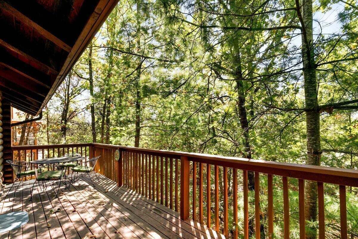 A wooden deck with a table and chairs, surrounded by a forest.
