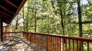 A wooden deck with a table and chairs, surrounded by a forest.