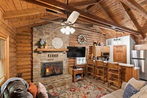 A log cabin interior with a fireplace, wooden furniture, a television, and a kitchen area. - Genuine Log Cabin, Jetted Tub, Gas Fireplace, Cmty Pools (Branson)