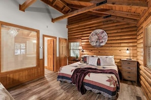 A log cabin bedroom with a bed, bedside table, and a wall-mounted clock. - Genuine Log Cabin, Jetted Tub, Gas Fireplace, Endless Community Amenities (Branson)