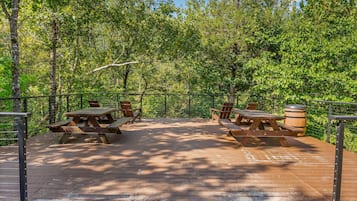An outdoor wooden deck with picnic tables and benches, surrounded by trees.