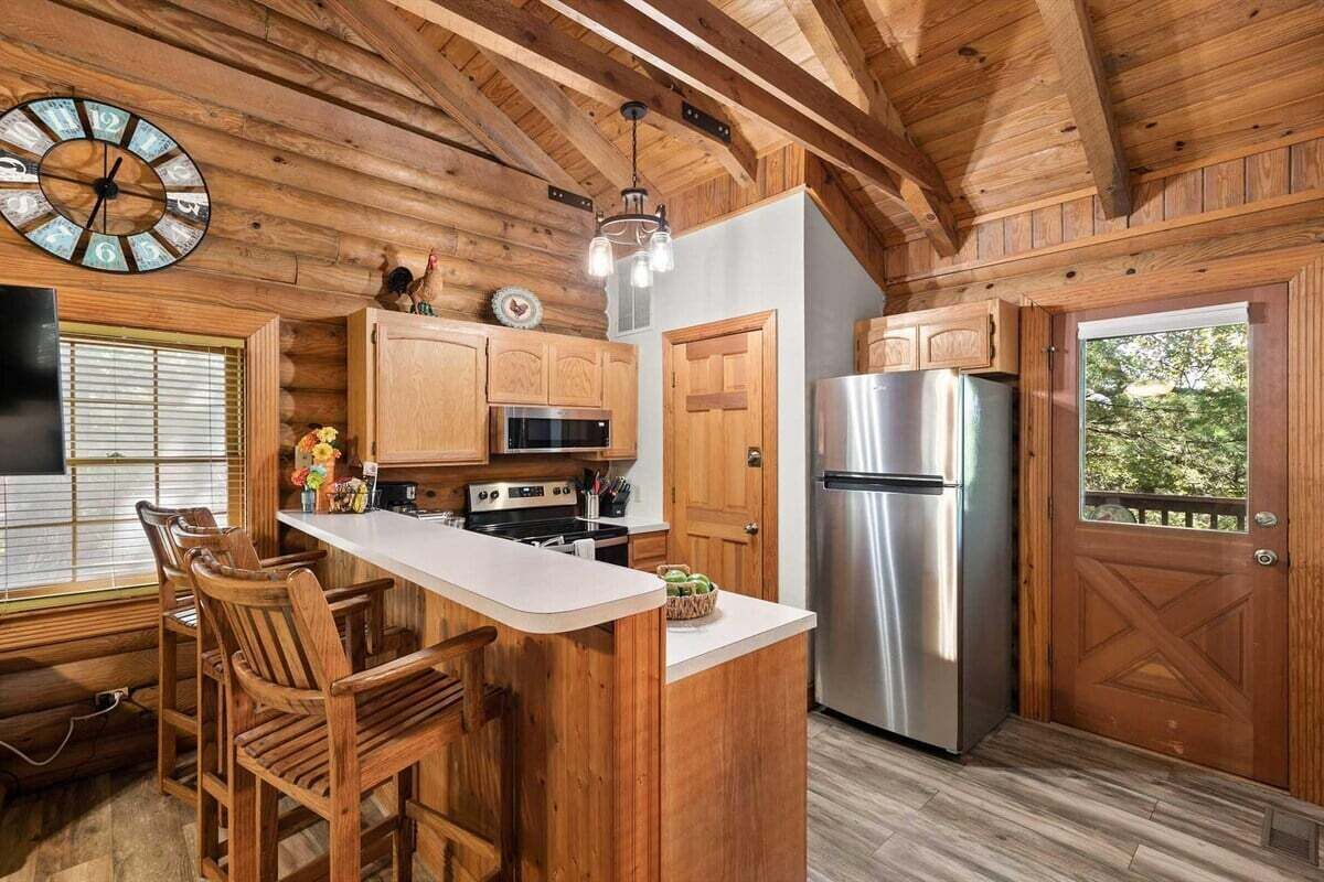 A kitchen with wooden cabinetry, a stainless steel refrigerator, and a bar area with stools.