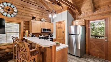 A kitchen with wooden cabinetry, a stainless steel refrigerator, and a bar area with stools.