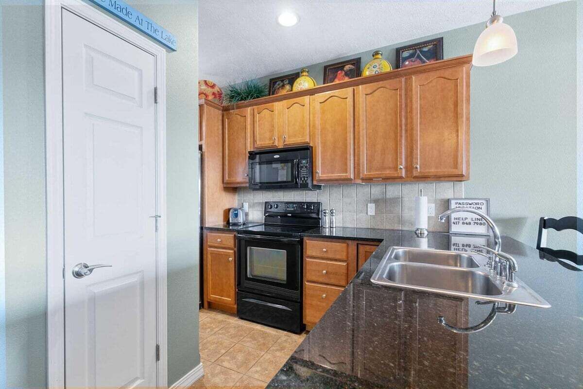A kitchen with wooden cabinets, a black stove, a microwave, and a stainless steel sink.