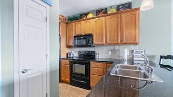A kitchen with wooden cabinets, a black stove, a microwave, and a stainless steel sink.