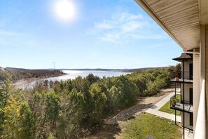 Een woongebouw met een balkon dat uitkijkt over een meer en een bebost gebied.