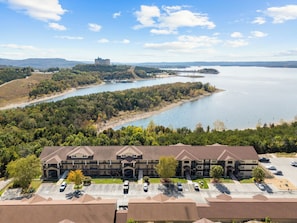 A multi-story hotel with a parking lot, surrounded by a lake and forested hills. - Majestic Condo on Table Rock Lake - Views for Mile- Free Daily Attraction Tickets (Branson)