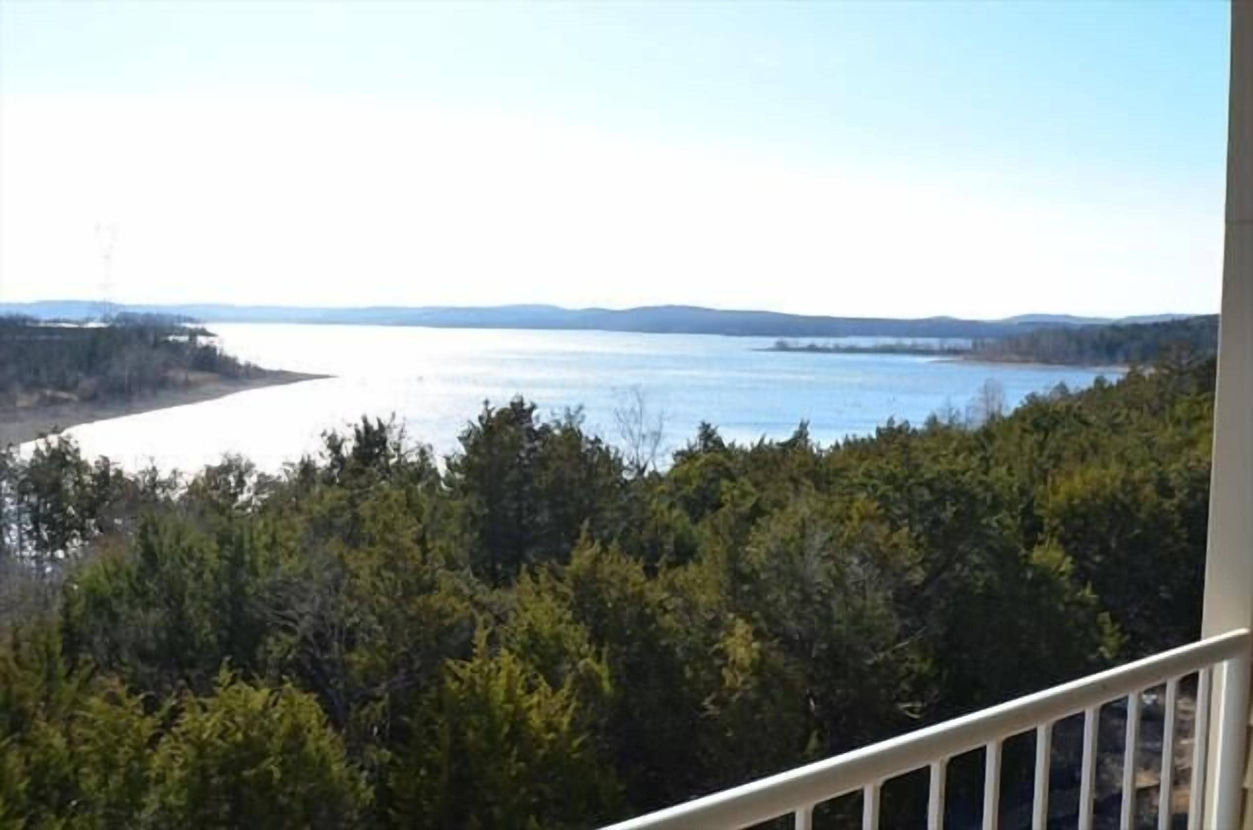A view from a balcony overlooking a body of water with dense forest in the foreground.