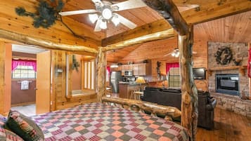 A log cabin interior with a bed, a fireplace, a kitchen, and a dining area.