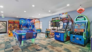 Habitación con máquinas de videojuegos arcade, incluyendo baloncesto y béisbol, piso alfombrado e iluminación empotrada en el techo.