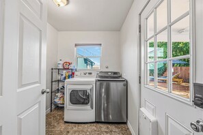 A compact laundry room with a washing machine, dryer, and a shelf with cleaning supplies. - 4BR Austin Backyard Oasis/Cowboy Pool + Fire Pit / Near Zilker, SoCo & Downtown (Austin)