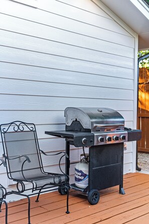 A barbecue grill with a gas tank and a metal chair on a wooden deck. - 4BR Austin Backyard Oasis/Cowboy Pool + Fire Pit / Near Zilker, SoCo & Downtown (Austin)