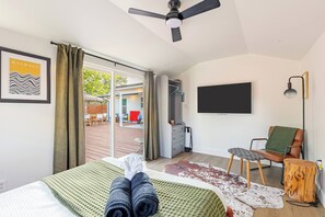Een hotelkamer met een bed, een televisie, een plafondventilator en uitzicht op buiten.