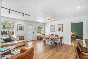 Een ruime woonkamer met houten vloer, een eettafel met stoelen, een bank en een salontafel.
