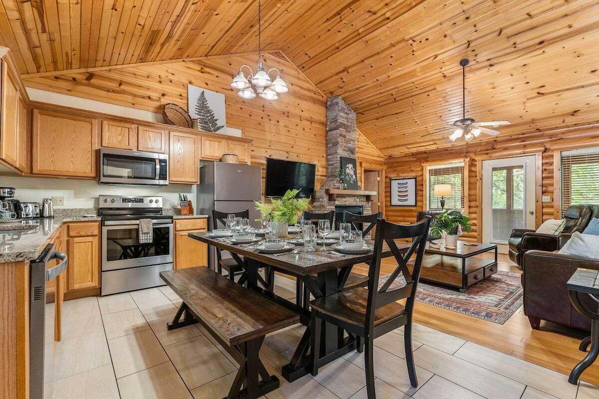 A cabin interior with a wooden interior, a dining area with a table set for four, a kitchen with modern appliances, and a fireplace.