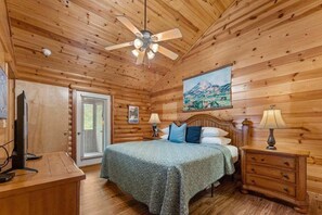 A wooden cabin bedroom with a bed, nightstands, a ceiling fan, and a painting on the wall. - Resort Family Cabin_Incredible Amenities_Free Daily Attraction Tickets (Branson)
