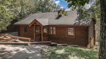 Une cabane rustique en rondins de bois, dotée d’une cheminée, d’un porche et d’une petite fenêtre.
