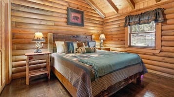 Une chambre dans un chalet en rondins, avec un lit, deux tables de chevet, une fenêtre avec des rideaux et un tableau encadré au mur.