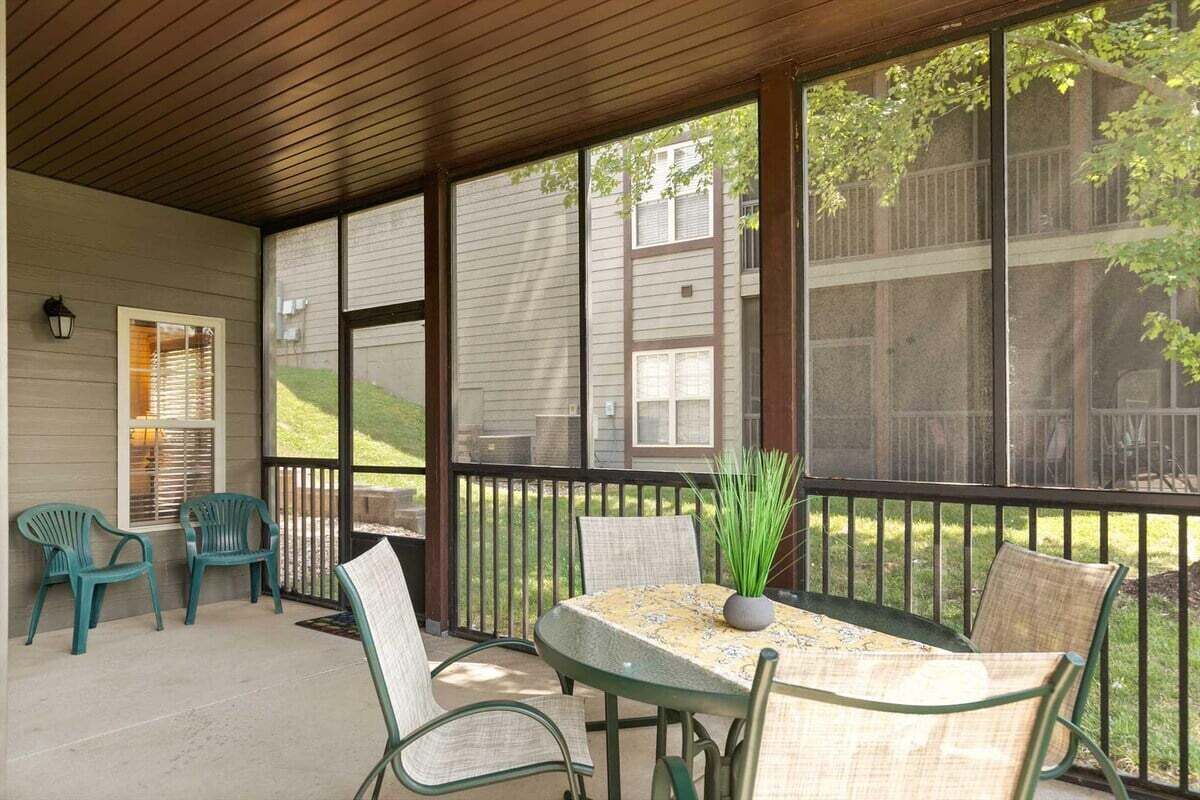 A covered patio with a table and chairs, a potted plant, and a view of a residential area.