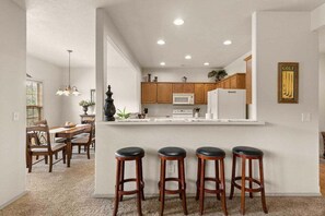 A modern kitchen with wooden cabinets, a white countertop, and a bar area with stools. - StoneBridge Villa-Near Silver Dollar City-Golf Course Views- Free Daily Attraction Tickets (Branson West)
