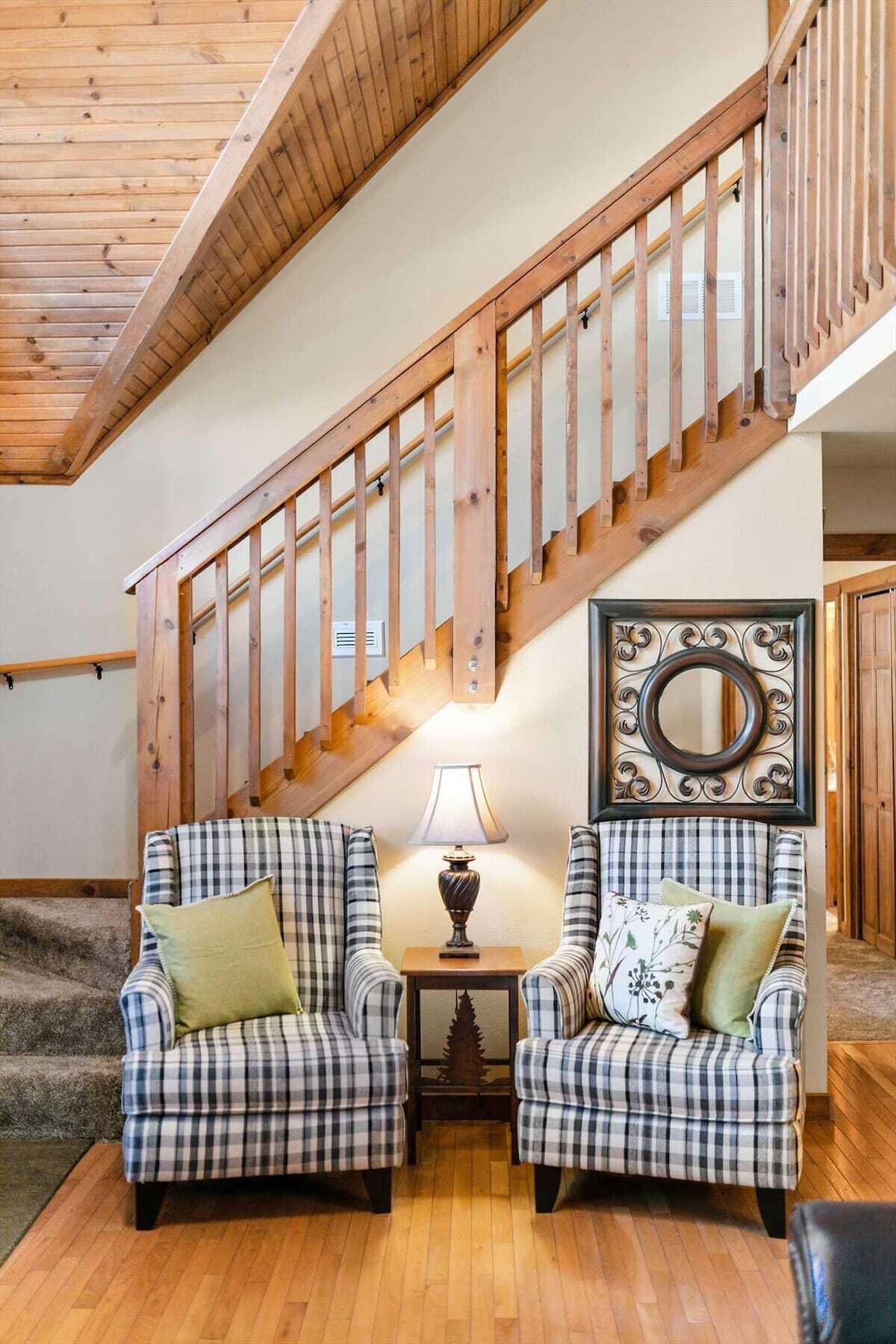 A staircase with wooden railings leading to an upper floor, flanked by two armchairs with plaid upholstery and a table with a lamp between them.