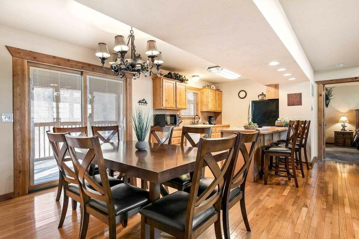 A dining area with a wooden table and chairs, a chandelier, and wooden cabinets in the background.