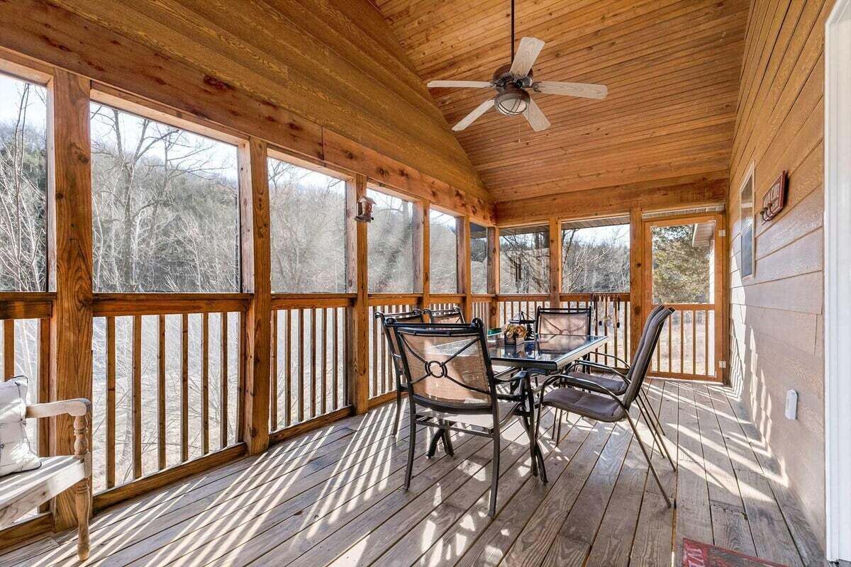 A covered outdoor area with a table and chairs, wooden deck, and a ceiling fan.
