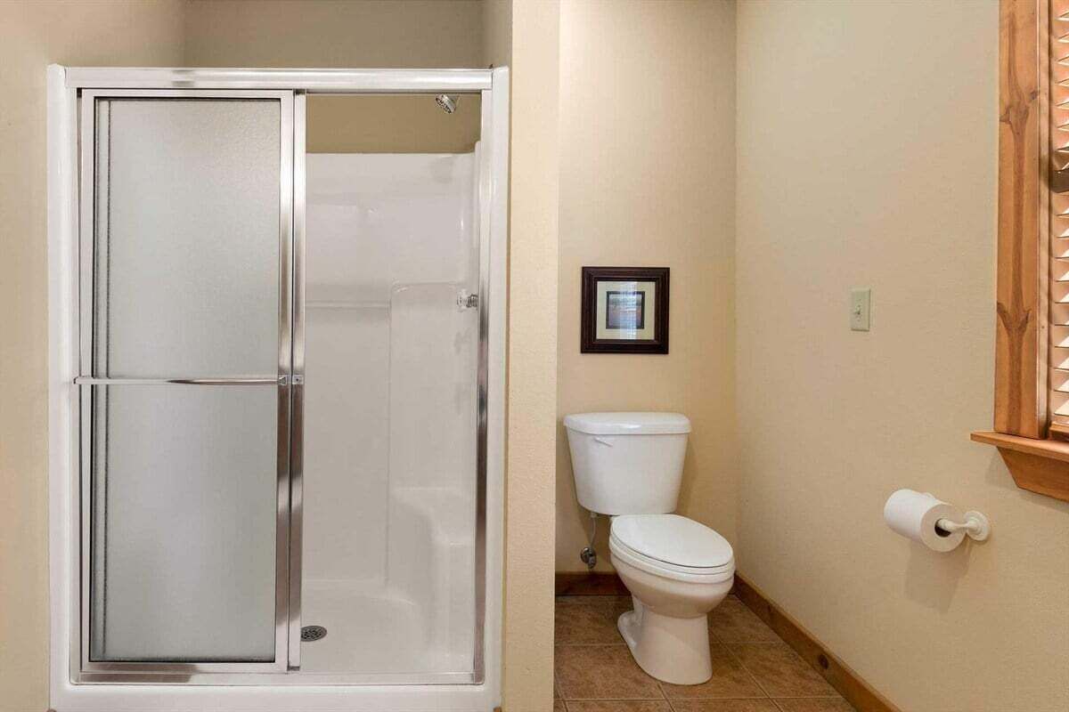 Een badkamer met een douchecabine van glas, een toilet en een ingelijst schilderij aan de muur.