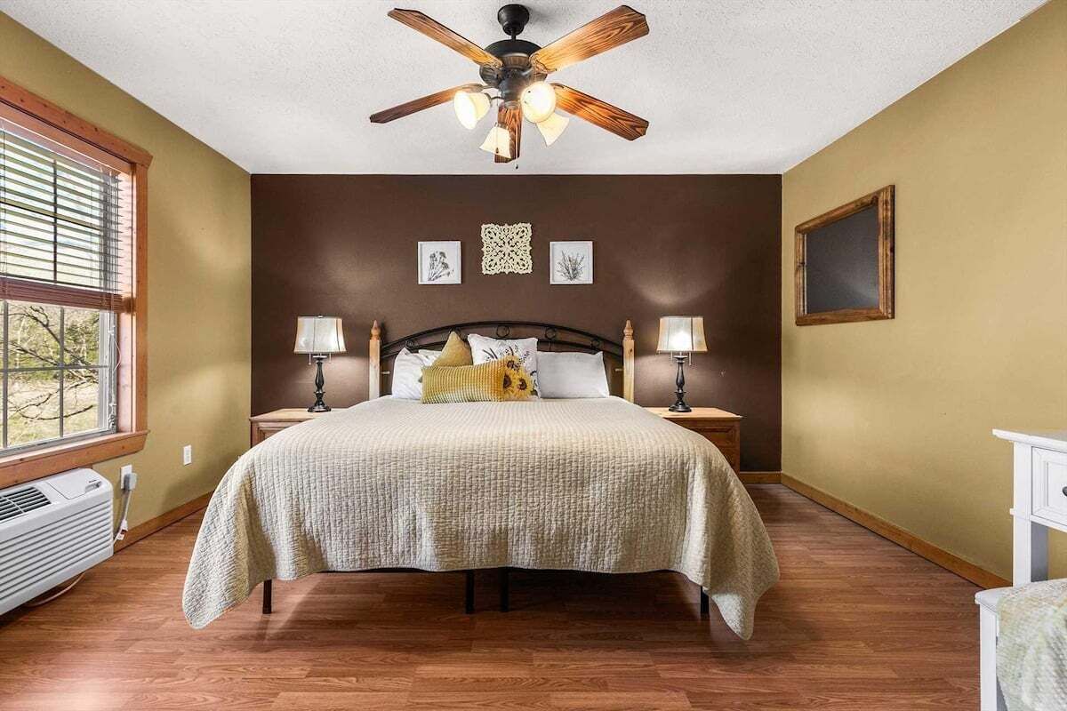 Een slaapkamer met een bed, twee nachtkastjes, een plafondventilator en een raam met zonwering.