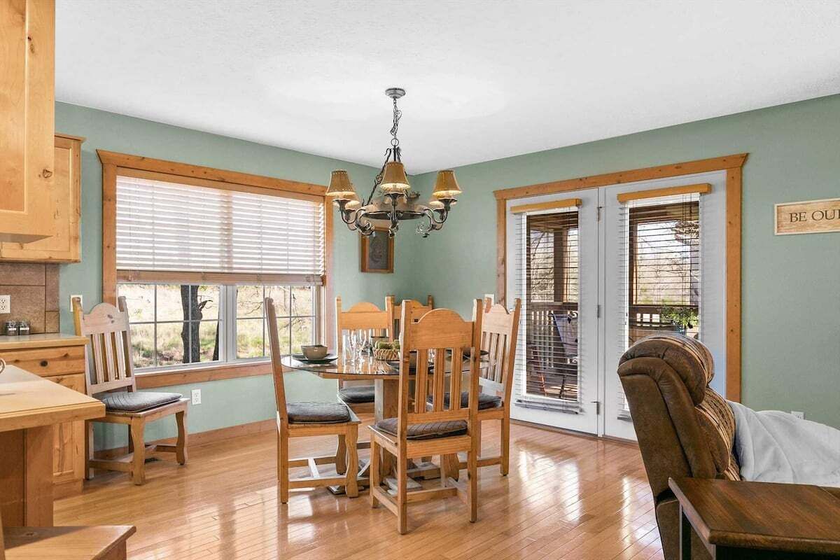 A dining area with wooden furniture, a chandelier, and a view through the windows.