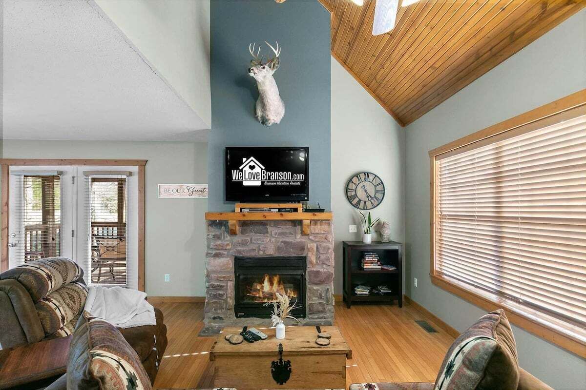 A living room with a fireplace, a mounted deer head, a television, and a clock.