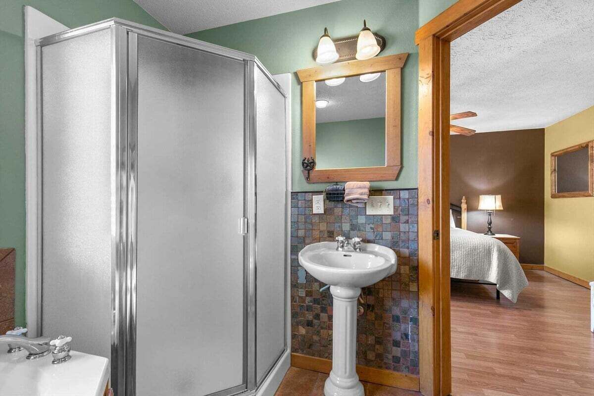 A bathroom with a walk-in shower, a pedestal sink, and a mirror above the sink.