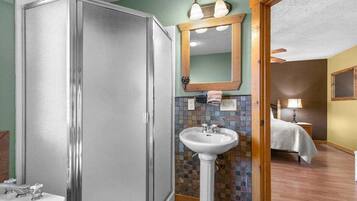 A bathroom with a walk-in shower, a pedestal sink, and a mirror above the sink.