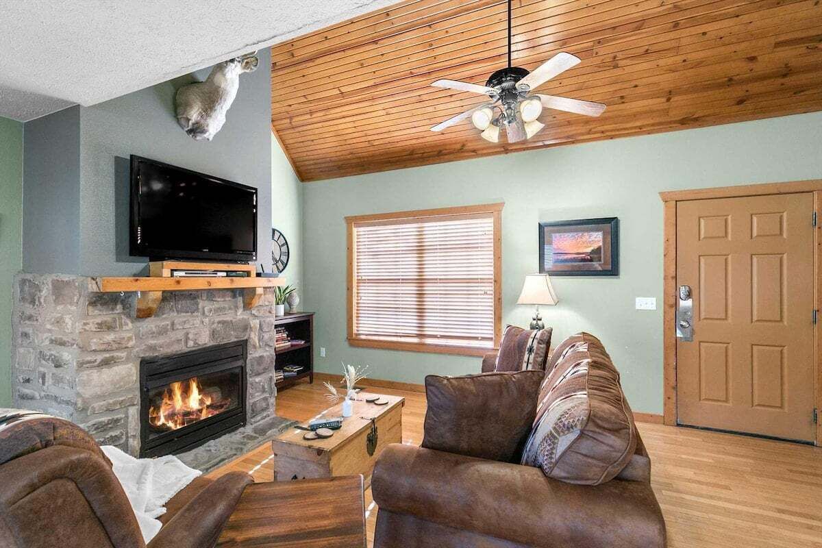 A living room with a stone fireplace, a television mounted above it, a ceiling fan, and a door to the right.