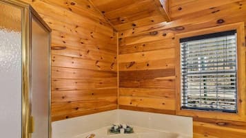 A wooden cabin interior with a large bathtub, a window with blinds, and a door with a glass panel.