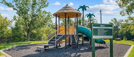 Ein Kinderspielbereich mit Rutsche, Klettergerüsten und überdachten Sitzgelegenheiten.