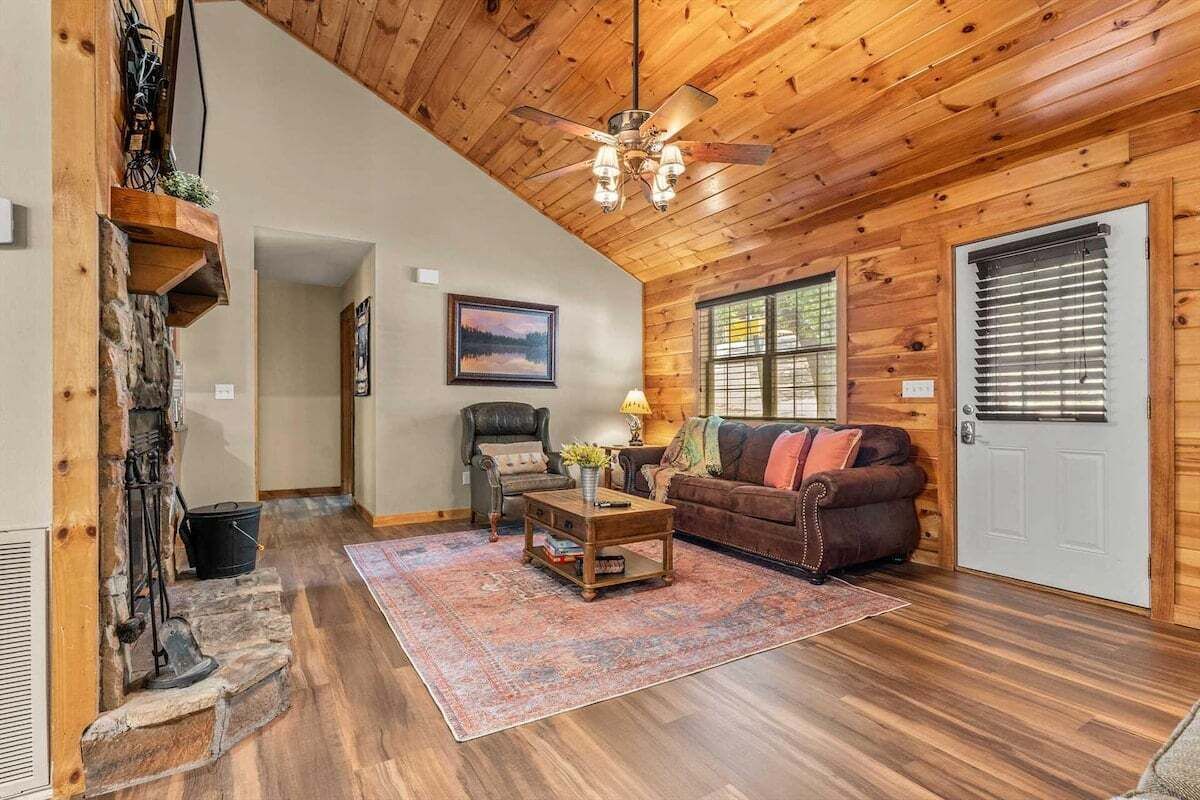 A wooden interior with a fireplace, a sofa, a coffee table, and a ceiling fan.