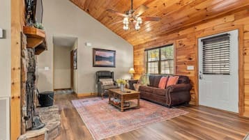 A wooden interior with a fireplace, a sofa, a coffee table, and a ceiling fan.