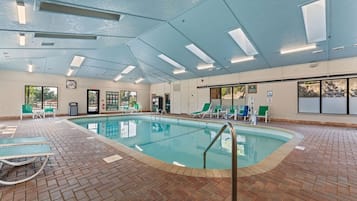 An indoor swimming pool with clear pool rules, a no diving sign, and a variety of lounge chairs around the pool area.