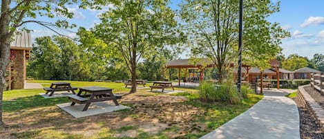 Un parque con mesas de picnic, un sendero para caminar y un edificio de fachada de piedra.