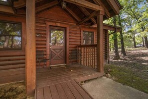 A log cabin with a porch, a door marked '153', and two chairs outside.