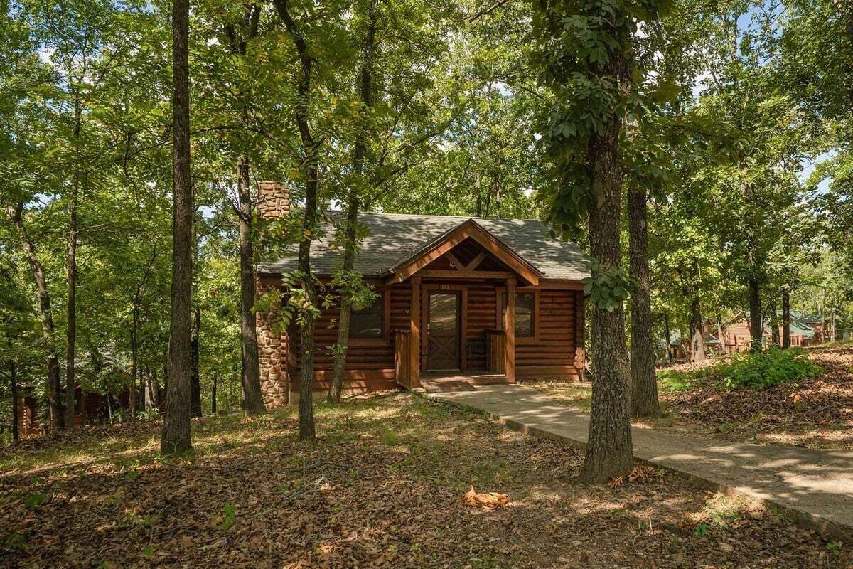 A rustic cabin with a stone foundation, surrounded by tall trees and a wooden deck.