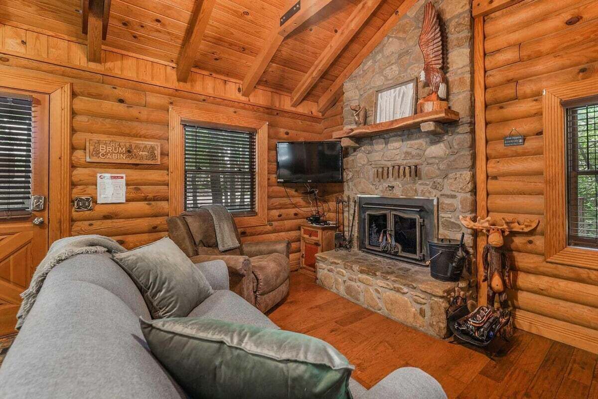 A log cabin interior with a stone fireplace, a television, and a couch.